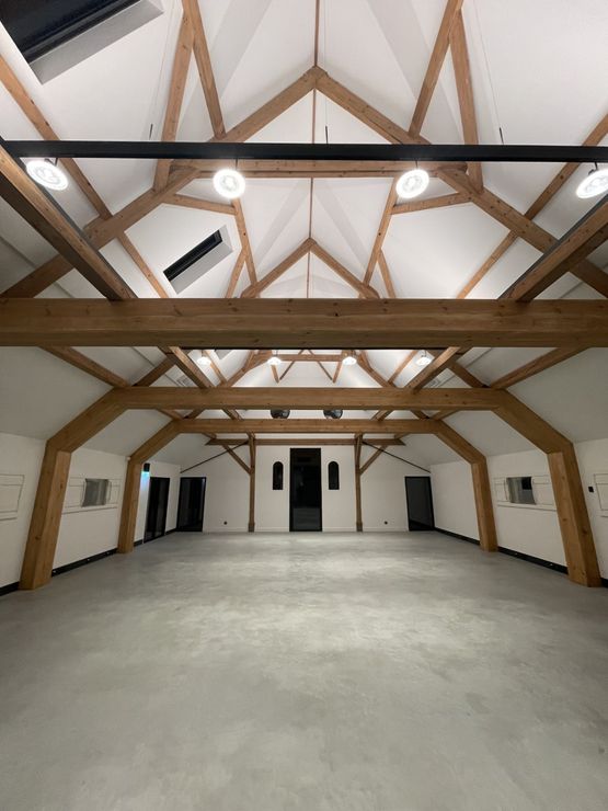 Een grote lege kamer met houten balken en witte muren.