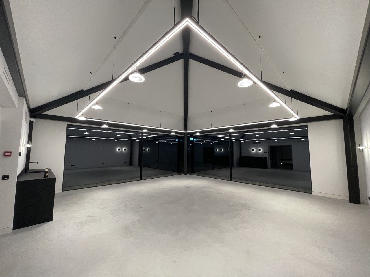 Een grote lege kamer met een driehoekige lamp die aan het plafond hangt.