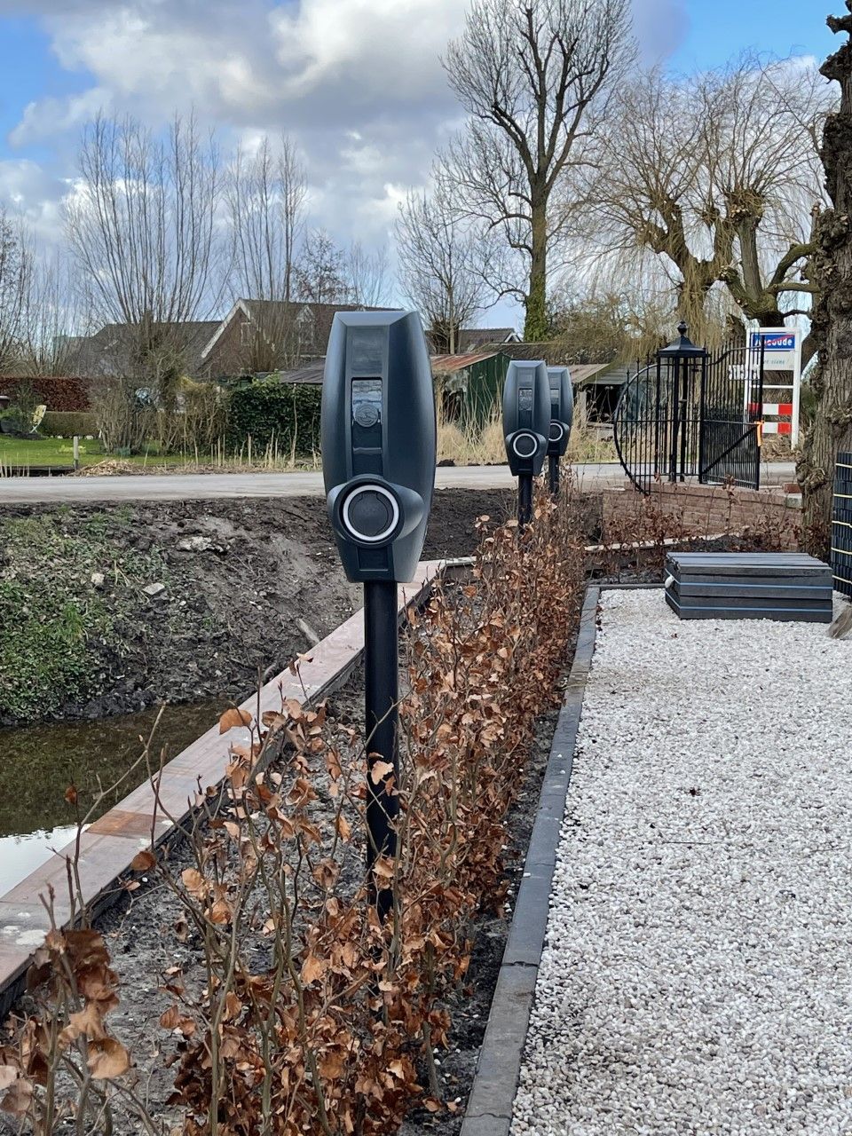 Een rij oplaadpunten voor elektrische voertuigen naast een grindpad.