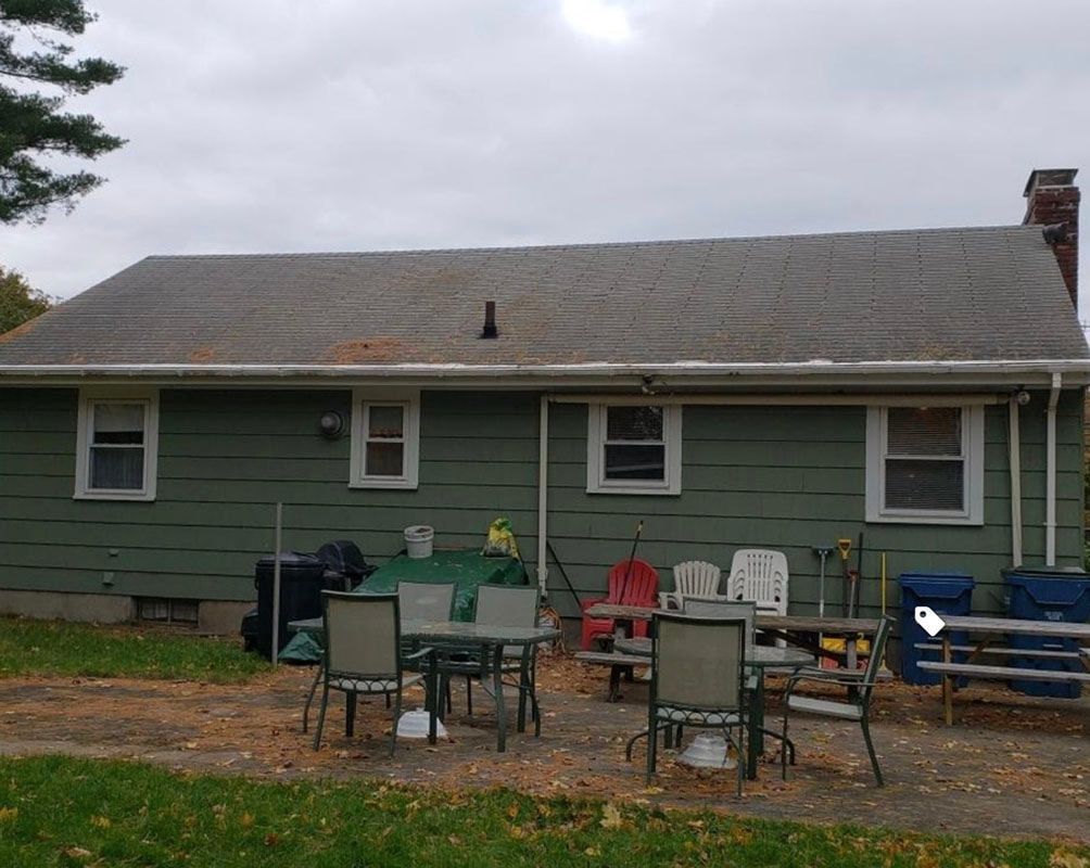 Green house with outdoor furniture on a patio in a backyard under a cloudy sky.