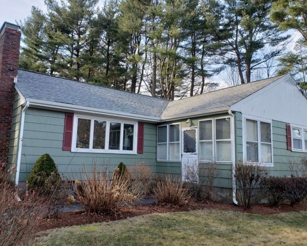 Green house with red shutters, brown brick chimney, and bare winter bushes.
