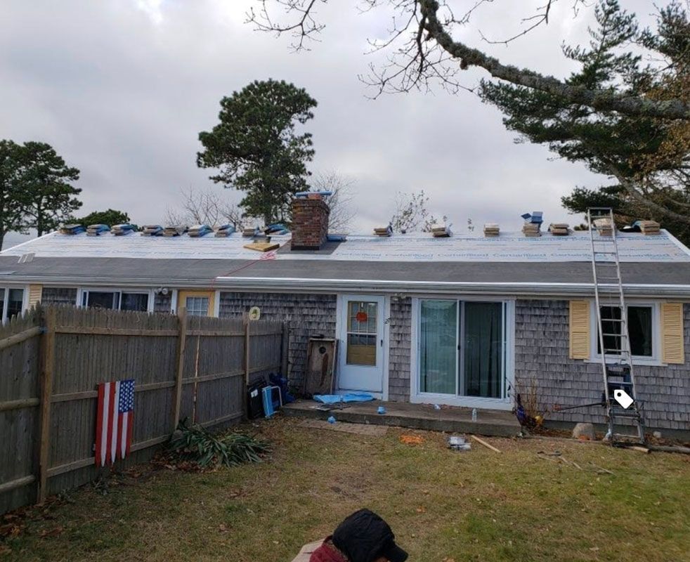 A house with a new roof under construction; a ladder leans against the side.