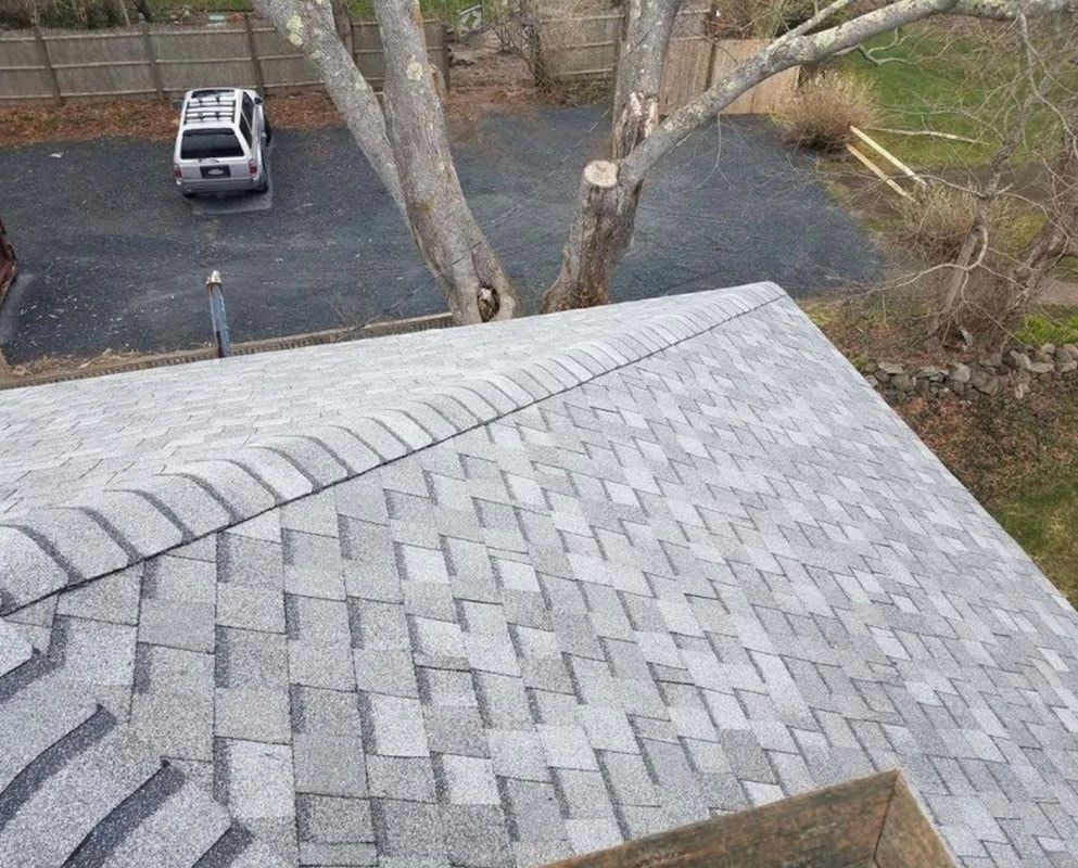 Gray shingled roof with a tree in the background, car parked in driveway.