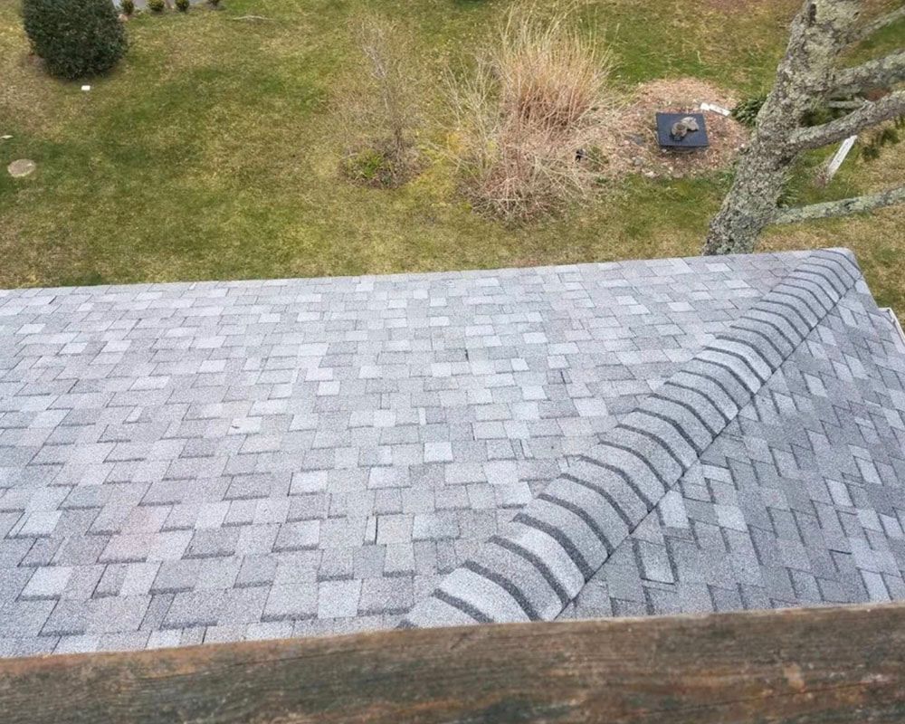 Gray shingled roof with curved ridge line; view overlooks grassy yard with a tree.