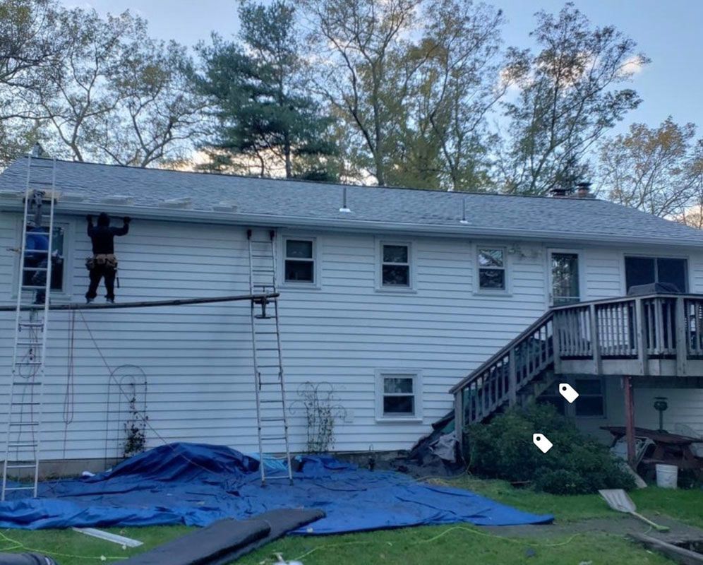 Roofer working on a white house roof. Ladder and scaffolding set up. Blue tarp on the ground.