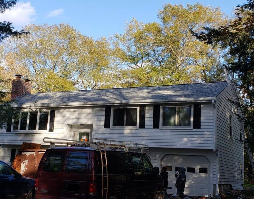White house with black shutters, trees in background. Red van in front.