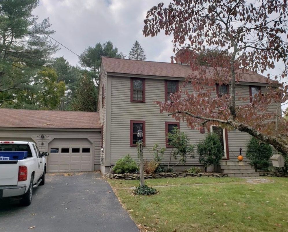 Two-story house with a garage and a truck in the driveway; a tree with red leaves is in front.