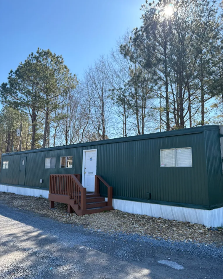 Armuchee Self Storage facility exterior in Rome, Georgia, featuring a green metal building with wooden entrance steps surrounded by pine trees Armuchee Self Storage facility exterior in Rome, Georgia, featuring a green metal building with wooden entrance steps surrounded by pine trees