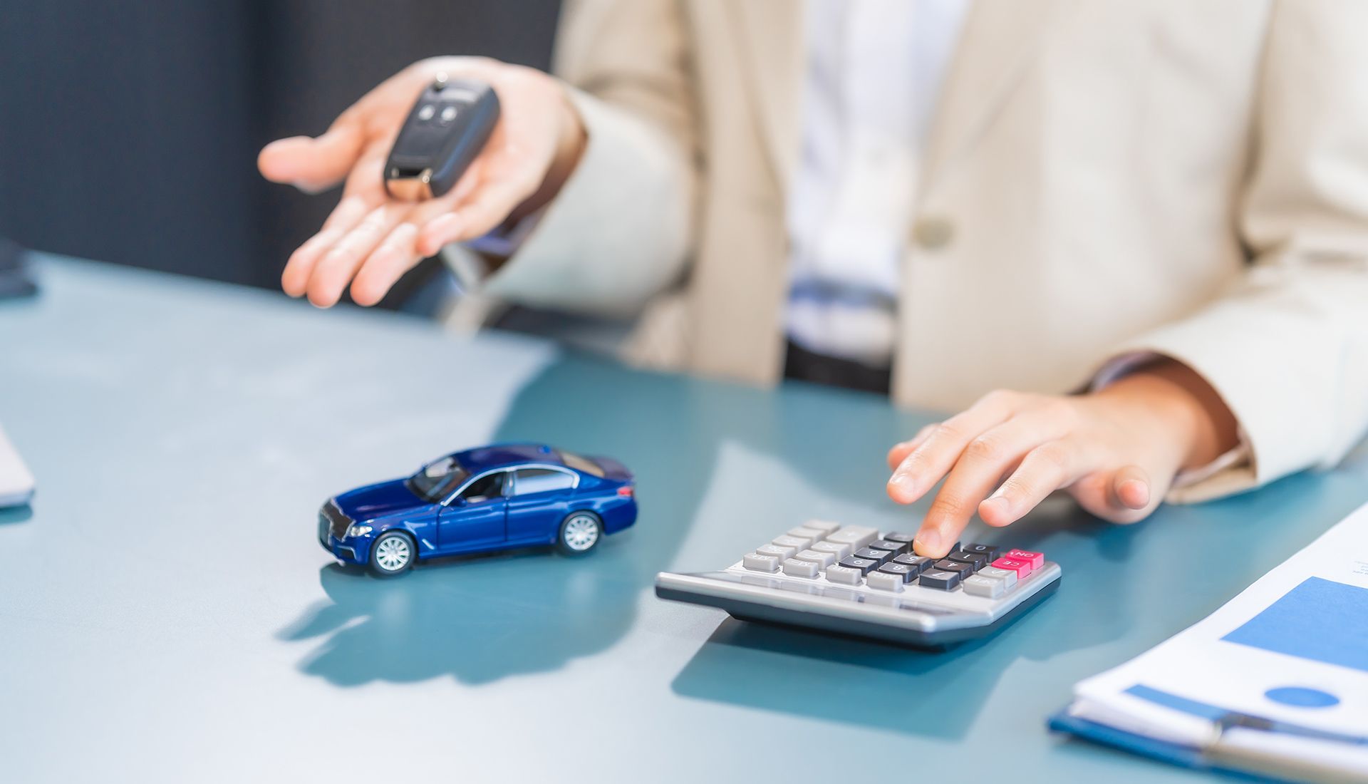 Person holding car keys, using calculator next to a toy car.