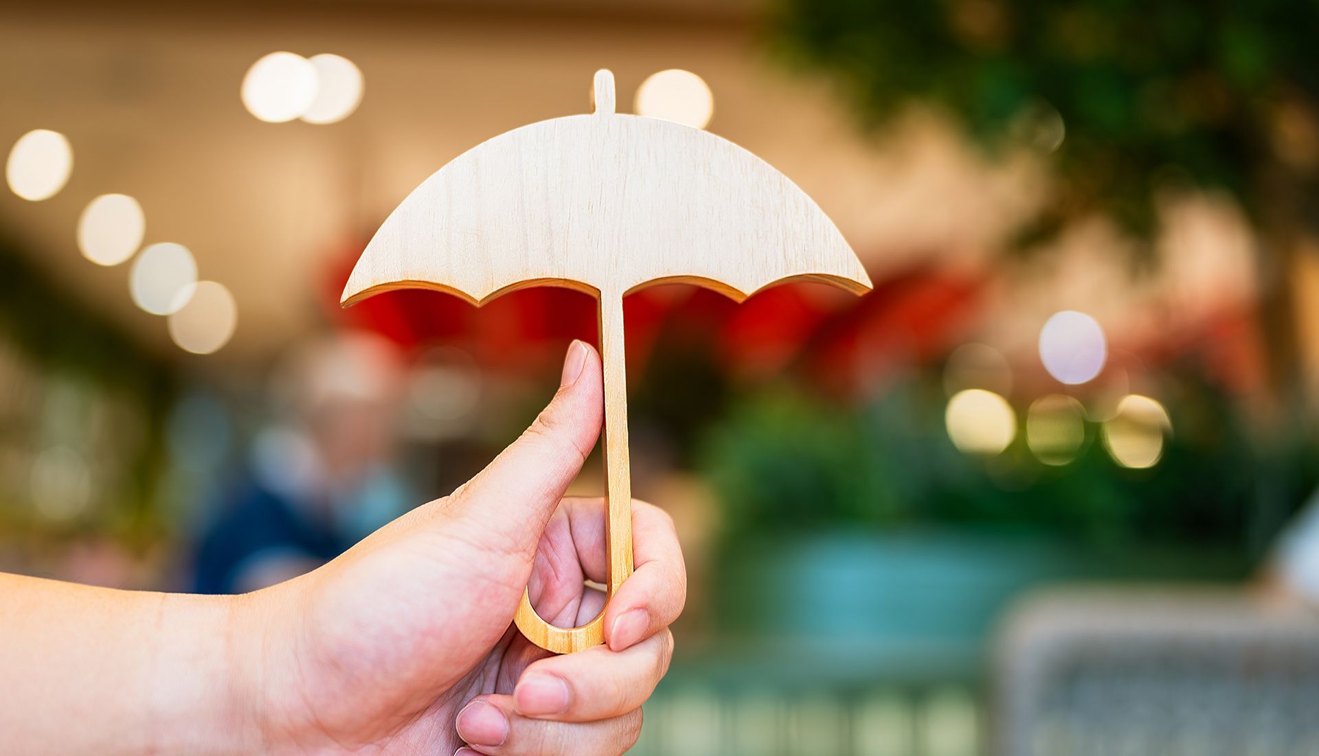 Hand holding a small wooden umbrella against a blurred background.