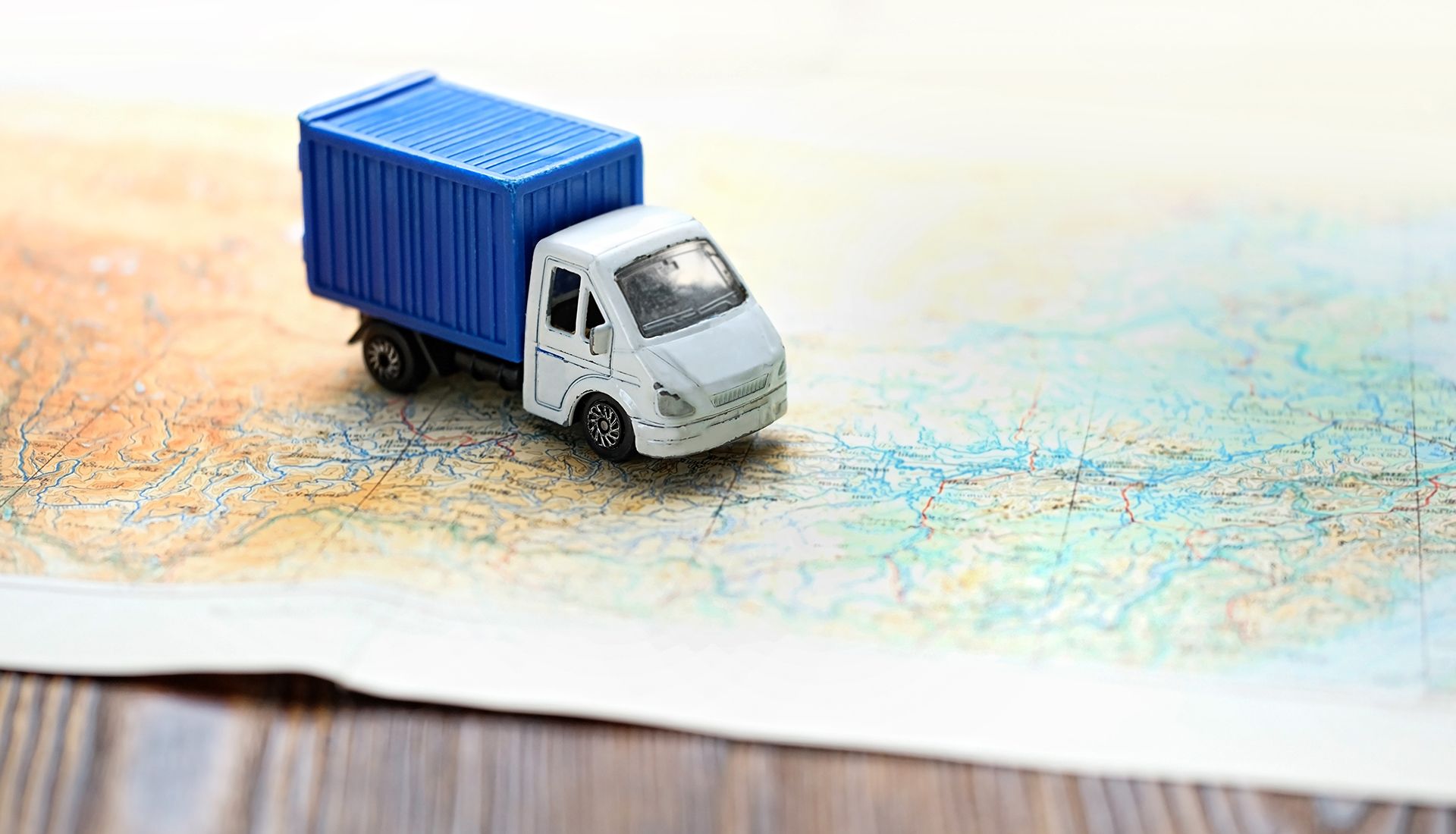 Toy truck on a map, white cab, blue container, brown and blue map.