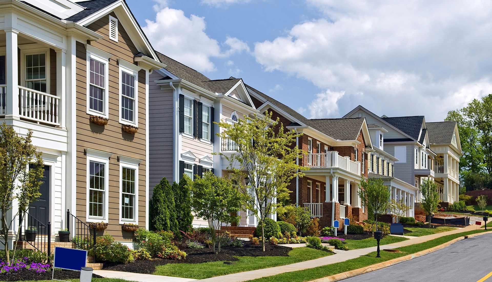 Row of colorful houses with porches and landscaping on a sunny street.