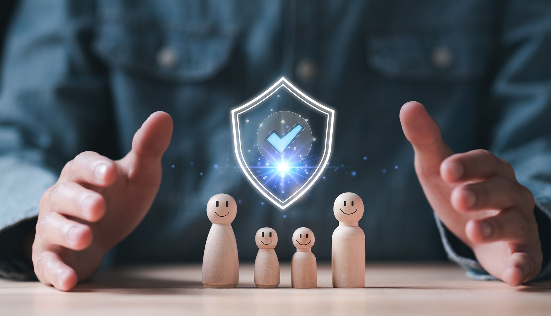 Hands protecting wooden family figures with a glowing shield graphic above them.