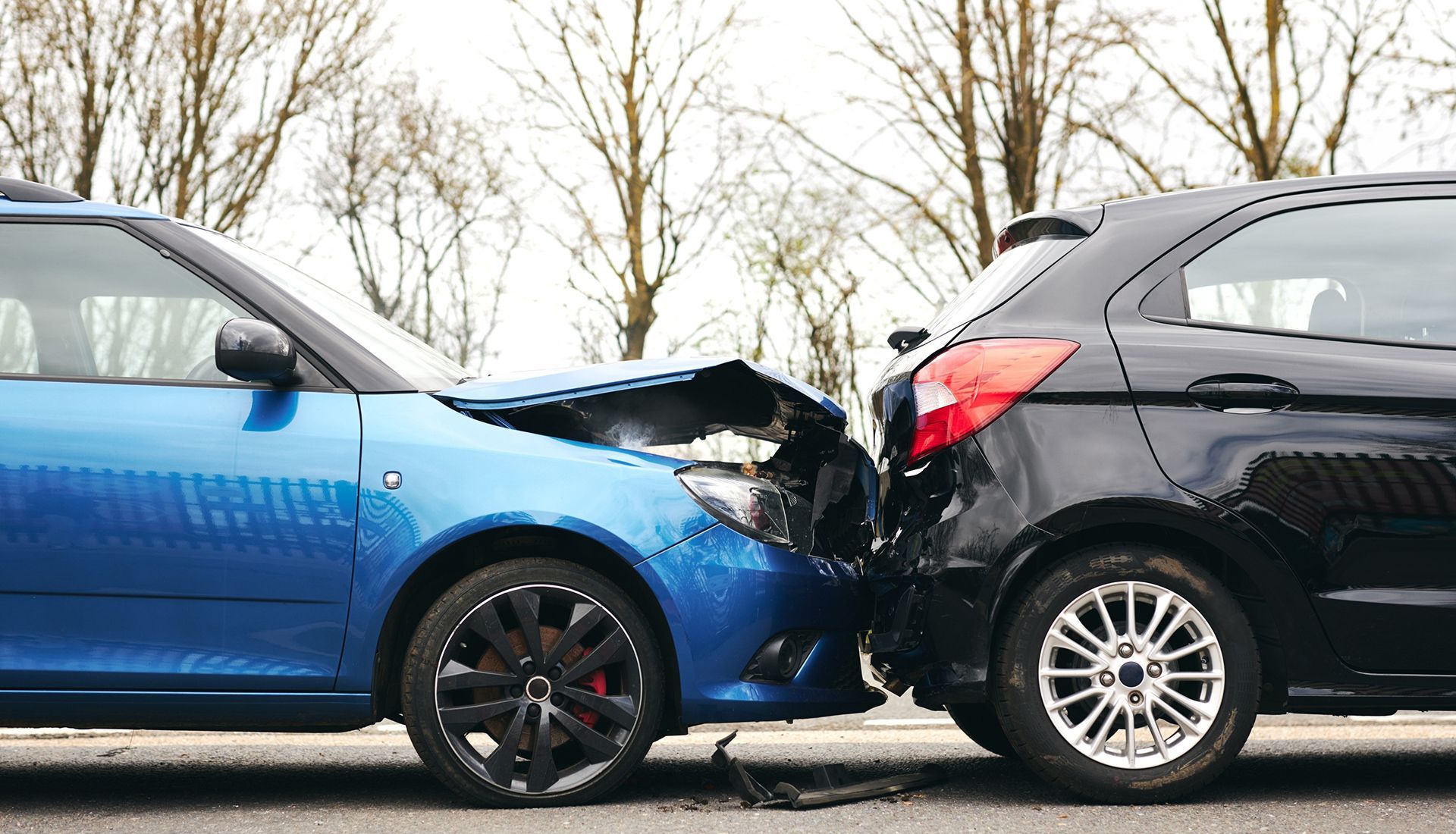 Blue car crashed into black car on a road.