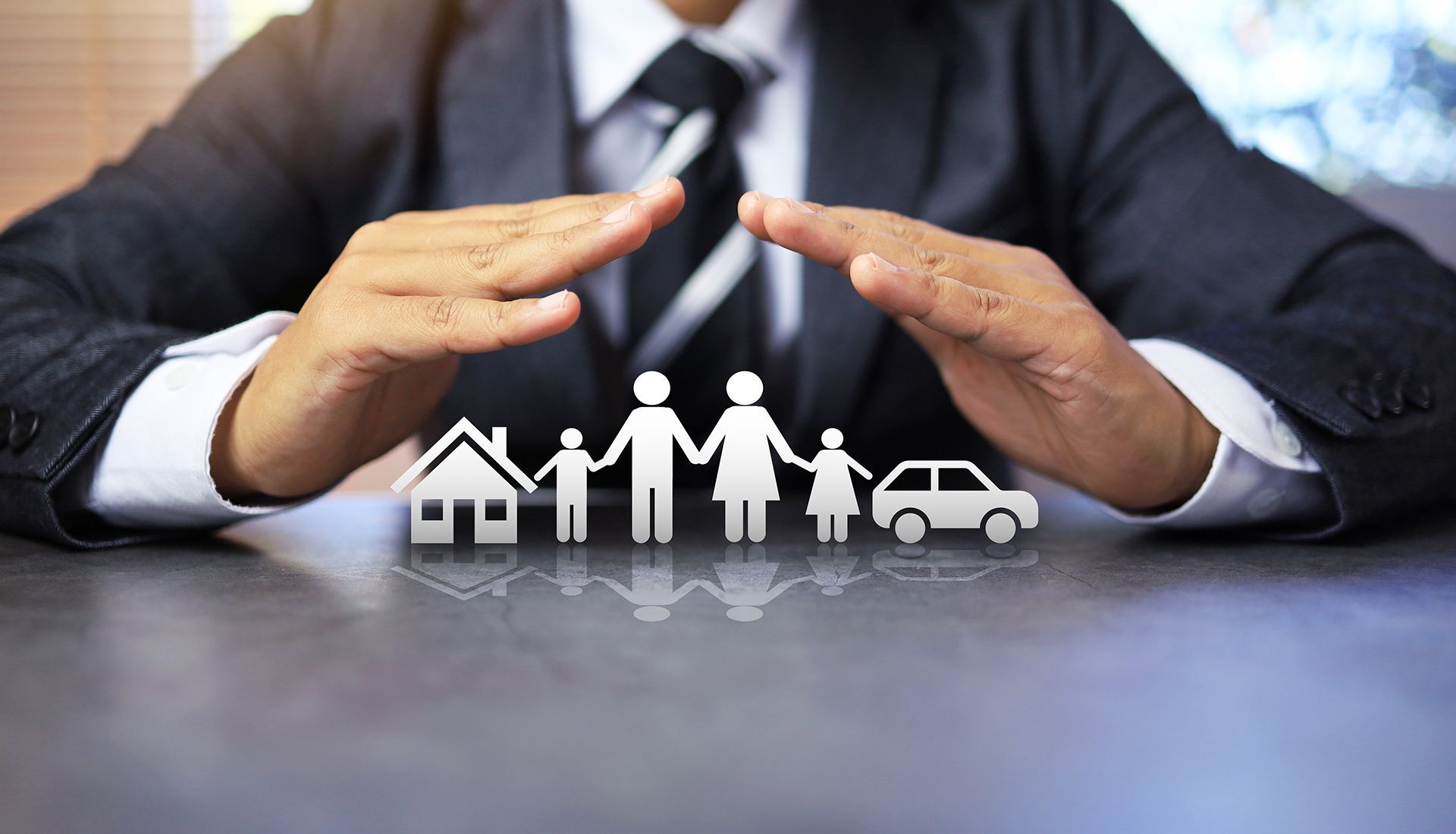 Person in suit protects family, house, and car cutouts with hands, symbolizing insurance or protection.