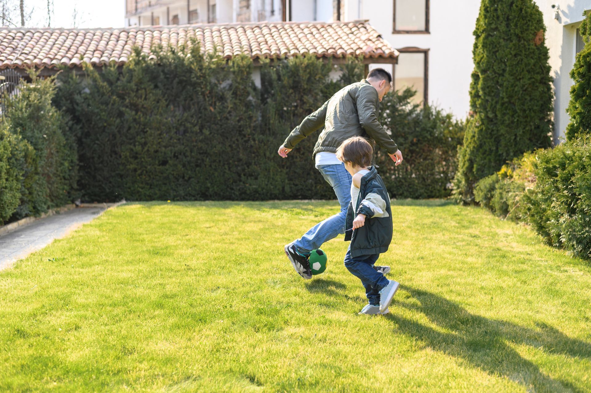 A man and a boy are playing soccer in a yard.