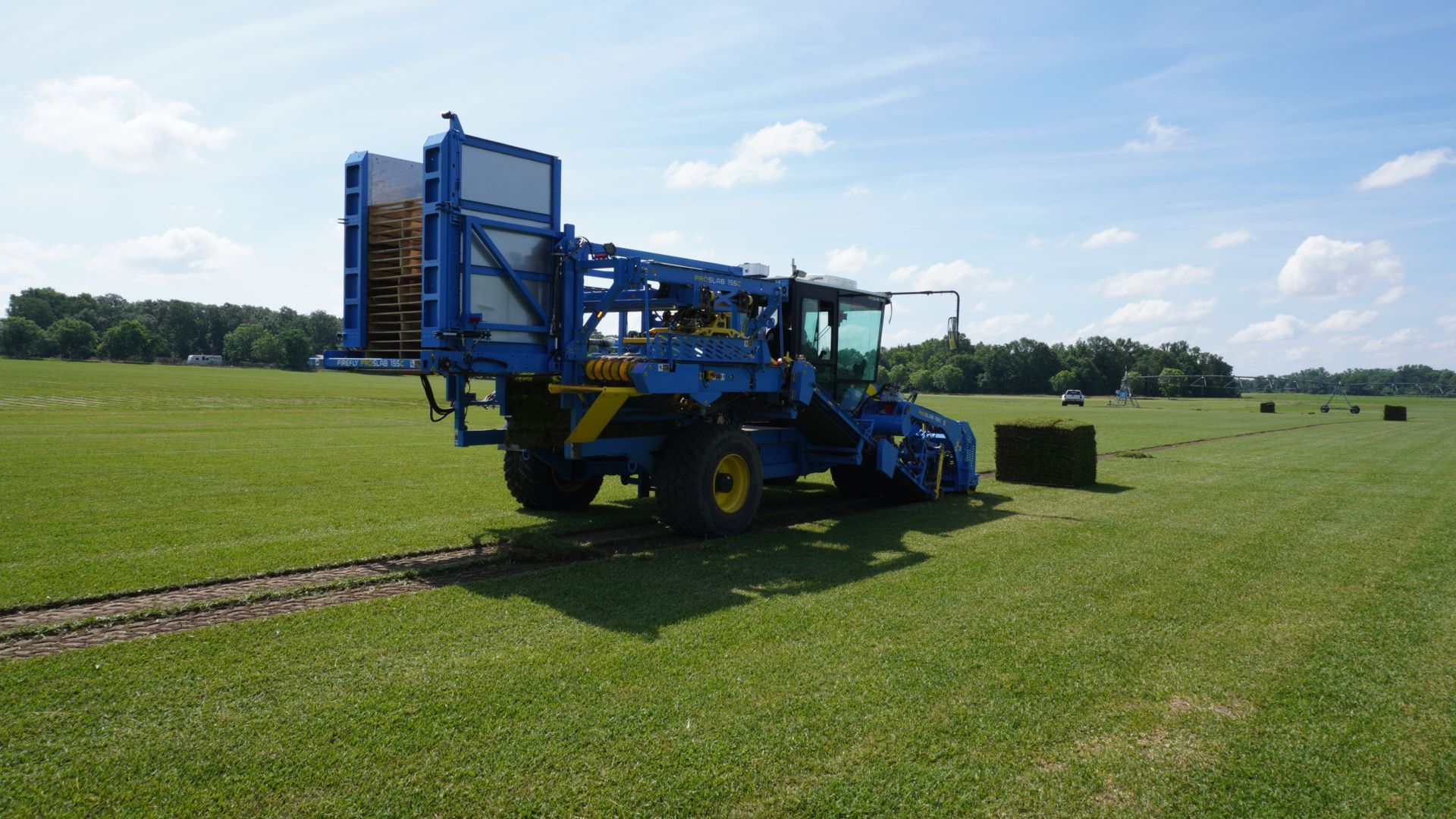 Blue agricultural machine on a grassy field under a sunny sky