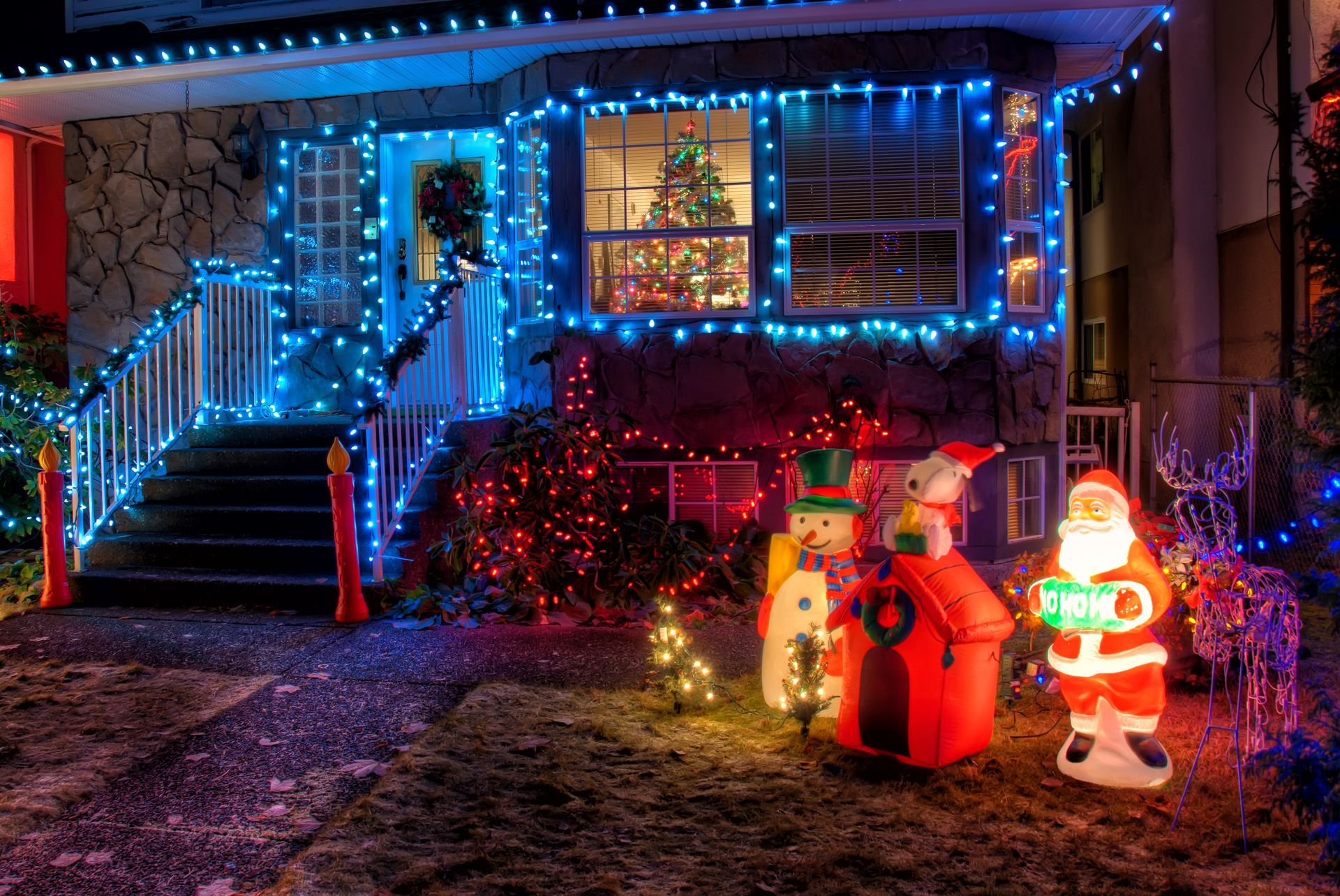 House with blue Christmas lights, steps, and lawn decorations including a snowman and Santa Claus.