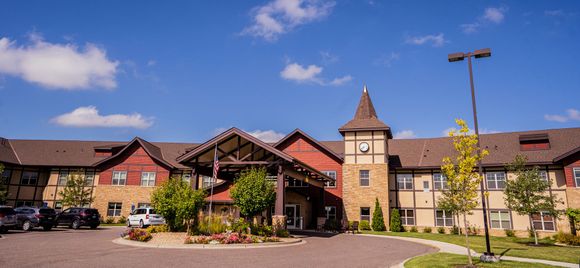 A multi-story hotel or lodge building with a central stone clock tower, wooden accents, and a large covered driveway.