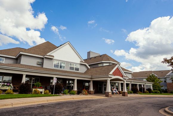 A low-angle view of a multi-story, grey-sided residential building with a covered entrance and a paved circular driveway.
