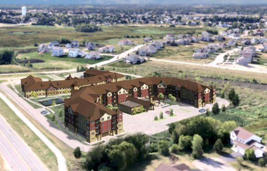 An aerial rendering shows a multi-story, brown-roofed apartment complex situated next to a road and a suburban neighborhood.