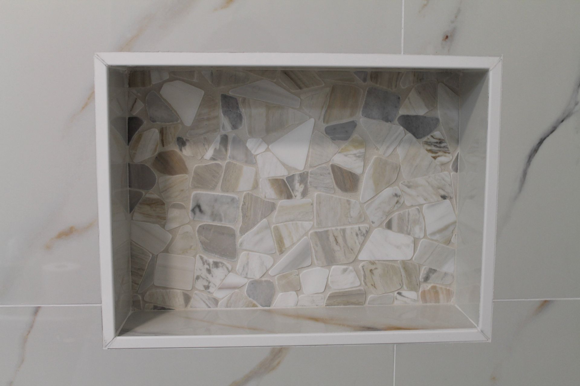 Modern white tile shower with niche with pebble mosaic and white grout