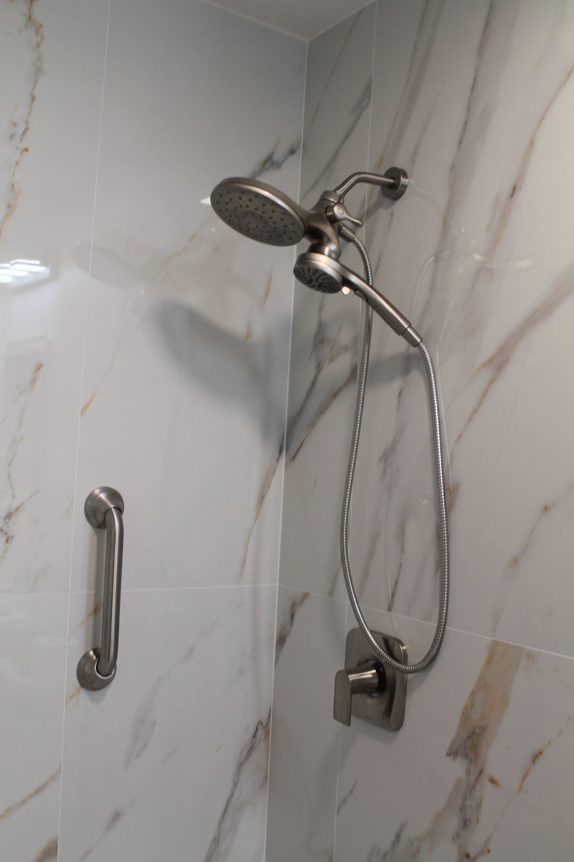 Modern white marble look large form tile shower with modern brushed stainless steel spa style showerhead with brushed silver accessibility handle