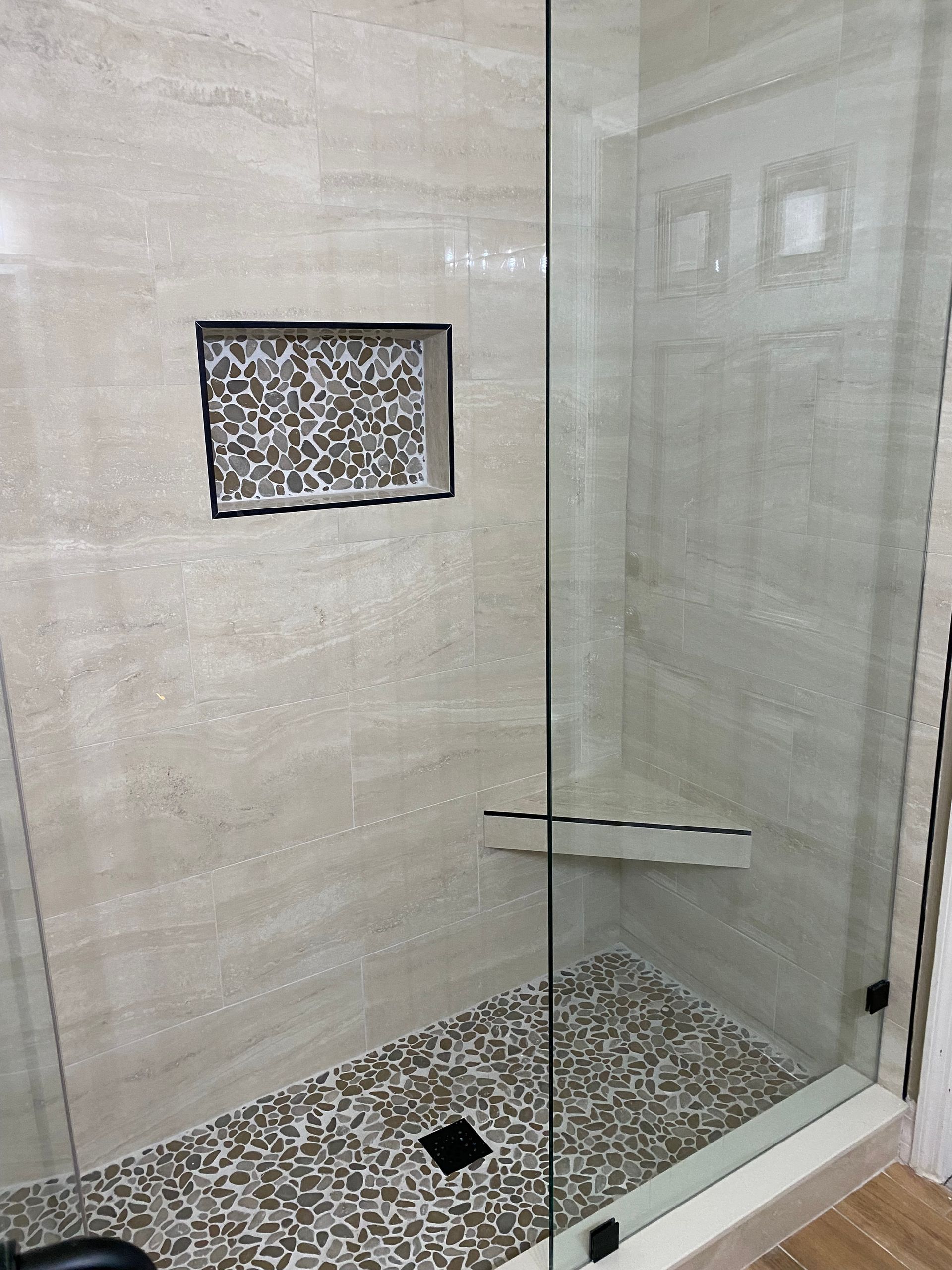 A walk in shower with a glass door and a tiled floor.
