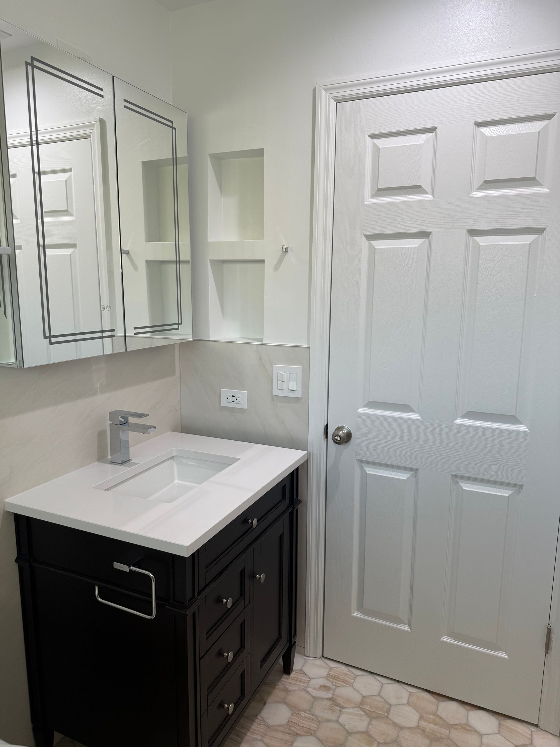 Remodeled bathroom vanity area with dark walnut cabinet, white quartz countertop, modern faucet, and mirrored medicine cabinet above beige wall tile.