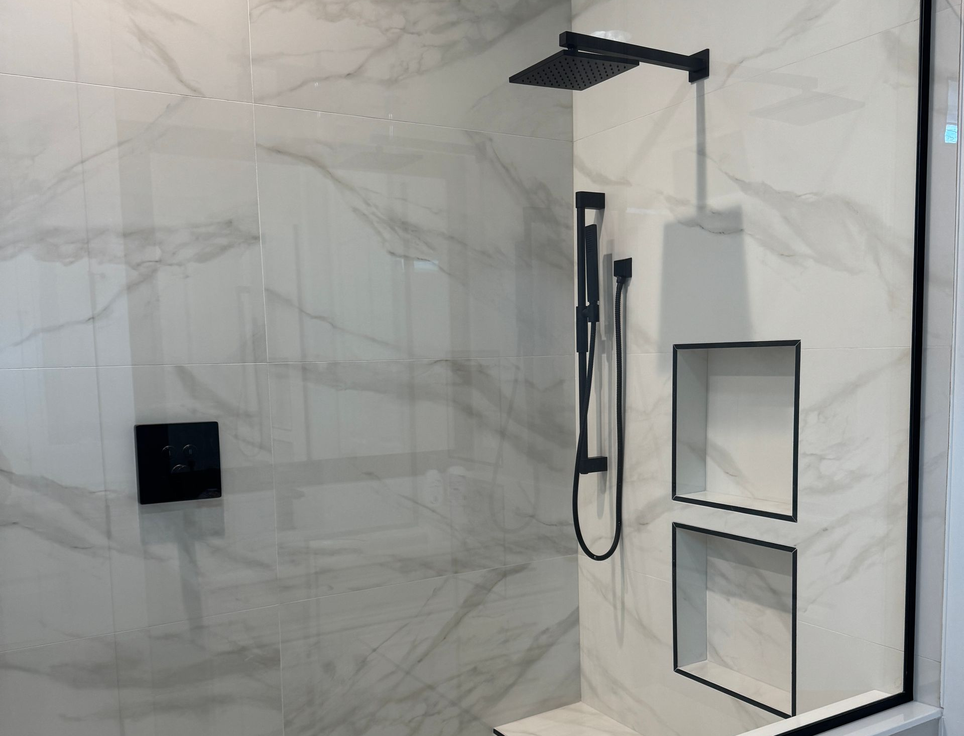 White large form tile bathroom with black trimming and shower head with niche