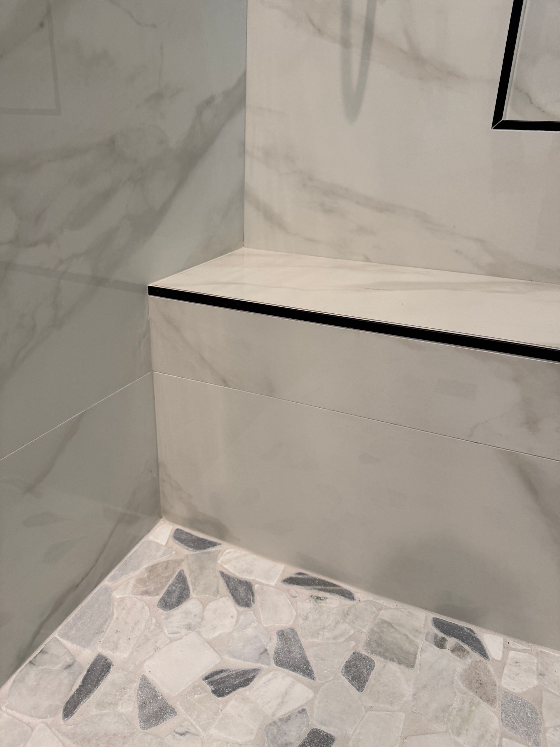 White large form tile bathroom with black trimming and shower head with niche