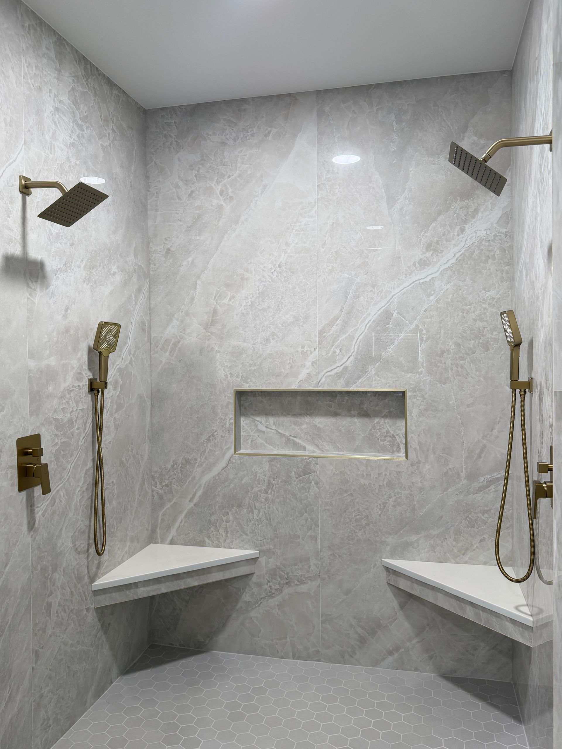 Symmetrical dual luxury tile shower, large format 110''x48'' grey matte tile, with built in niche, dual shower heads , dual tile and quartz bench, large niche, luxury floor with brushed gold hardware