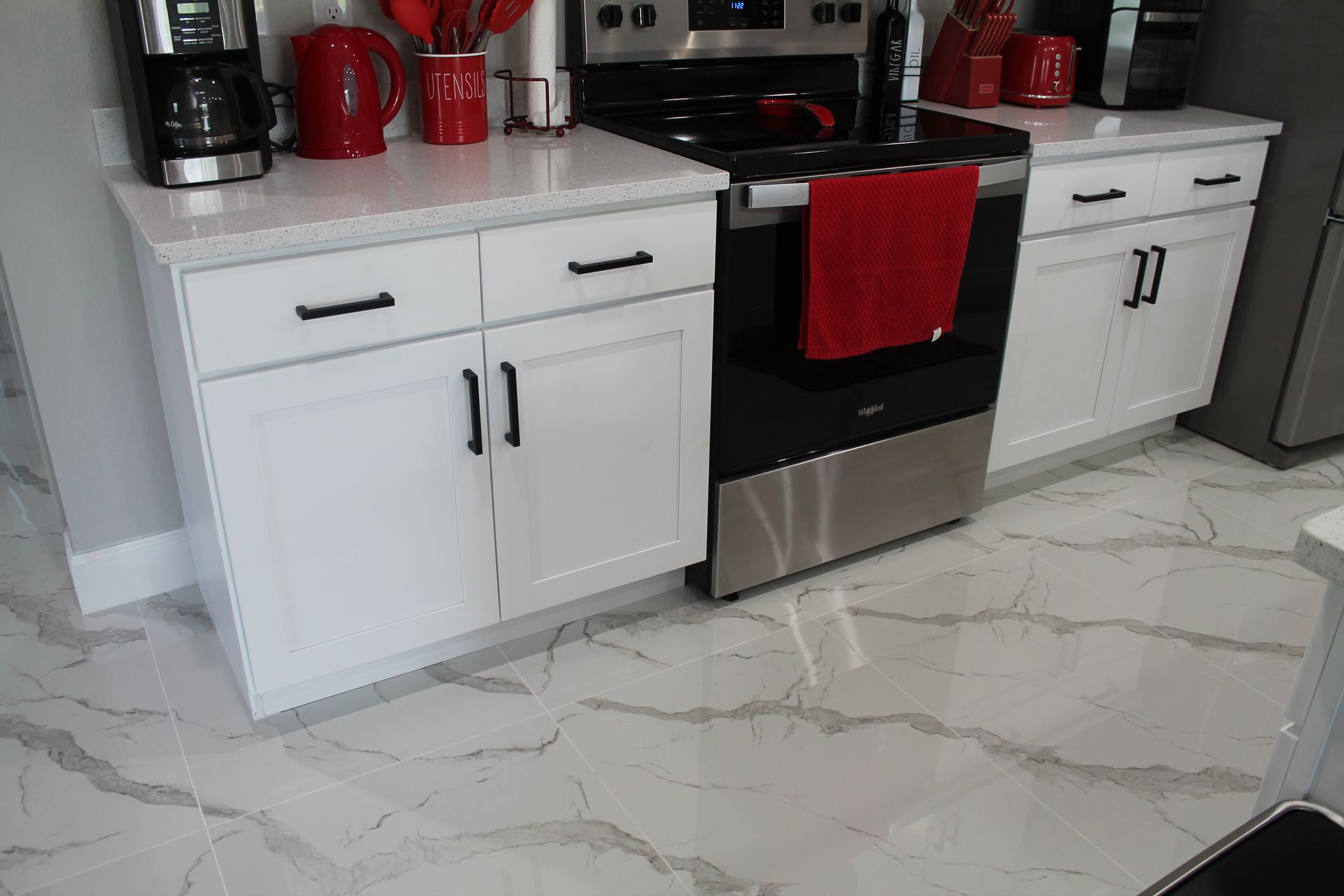 White shaker cabinets with matte black accents red decoration and white tile flooring