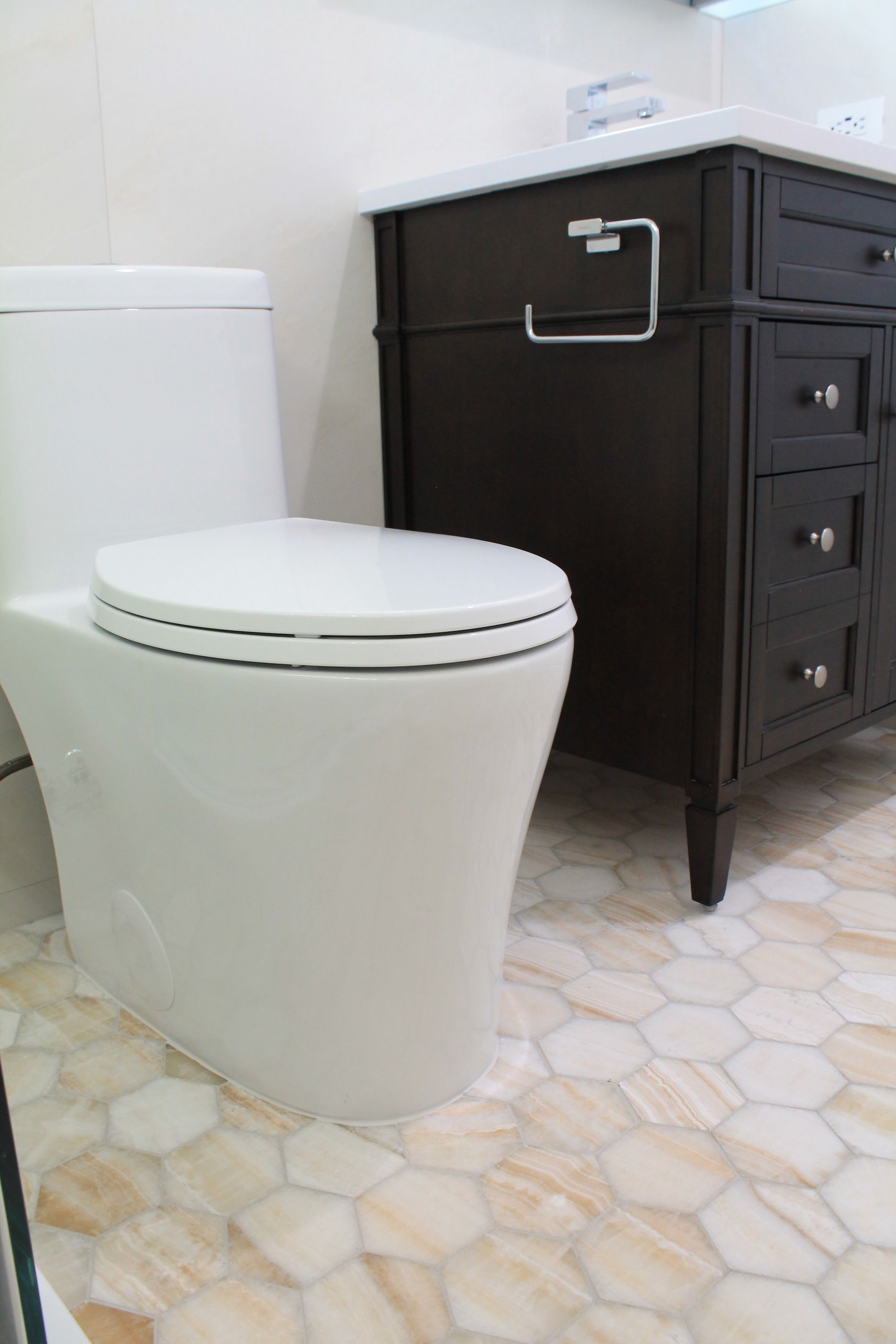 Bathroom remodel featuring a white toilet, hexagon beige-orange tile flooring, glass shower enclosure, and dark walnut vanity with quartz countertop.