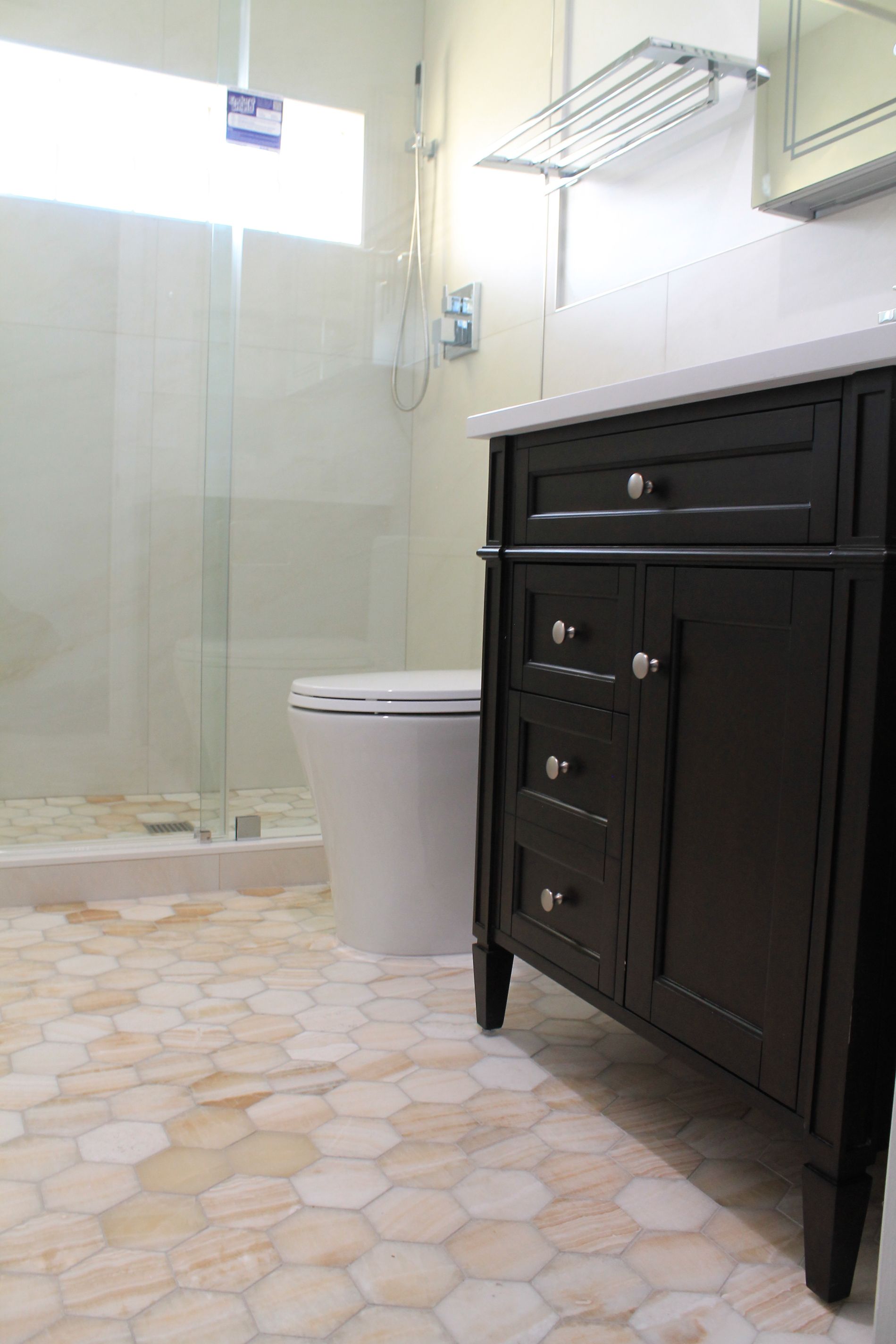 Bathroom remodel featuring a white toilet, hexagon beige-orange tile flooring, glass shower enclosure, and dark walnut vanity with quartz countertop.