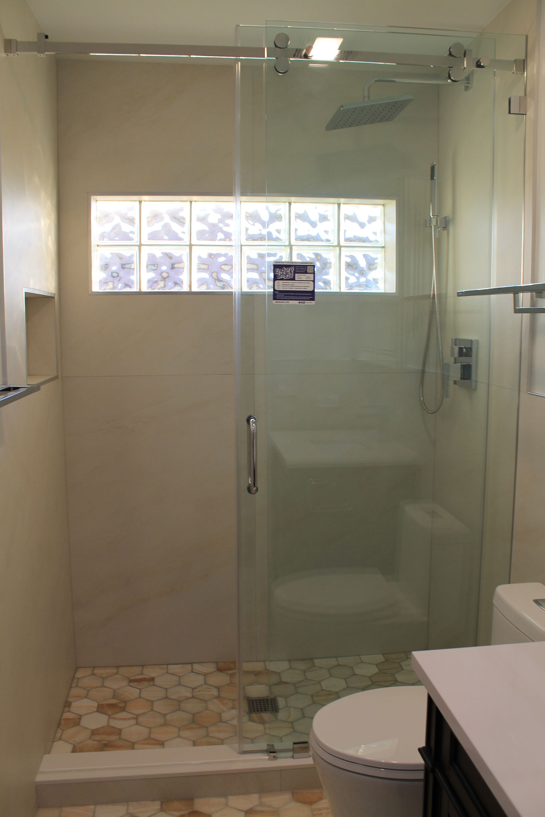 Updated bathroom shower with sliding glass door, rainfall shower head, beige wall tile, and hexagon beige-orange tile floor
