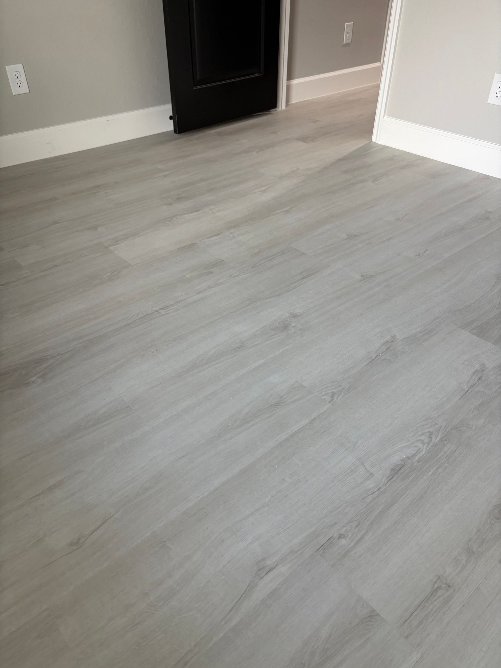 A room with a gray hardwood floor and a black door.