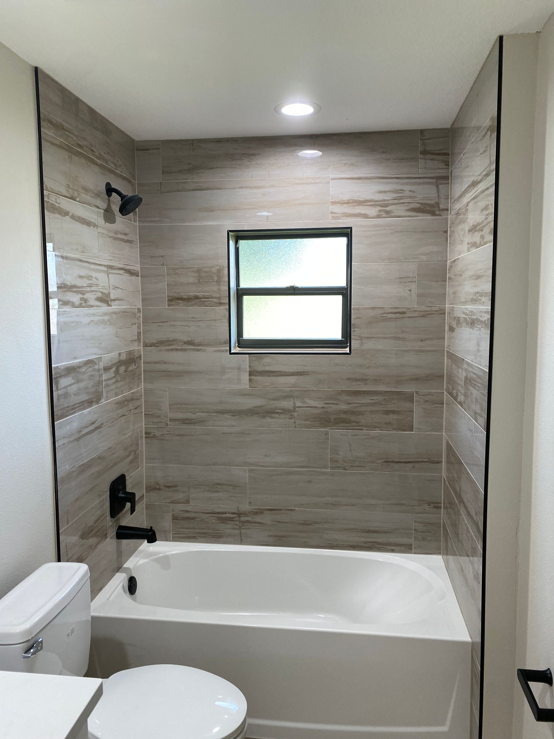 A bathroom with a tub , toilet , shower and window.