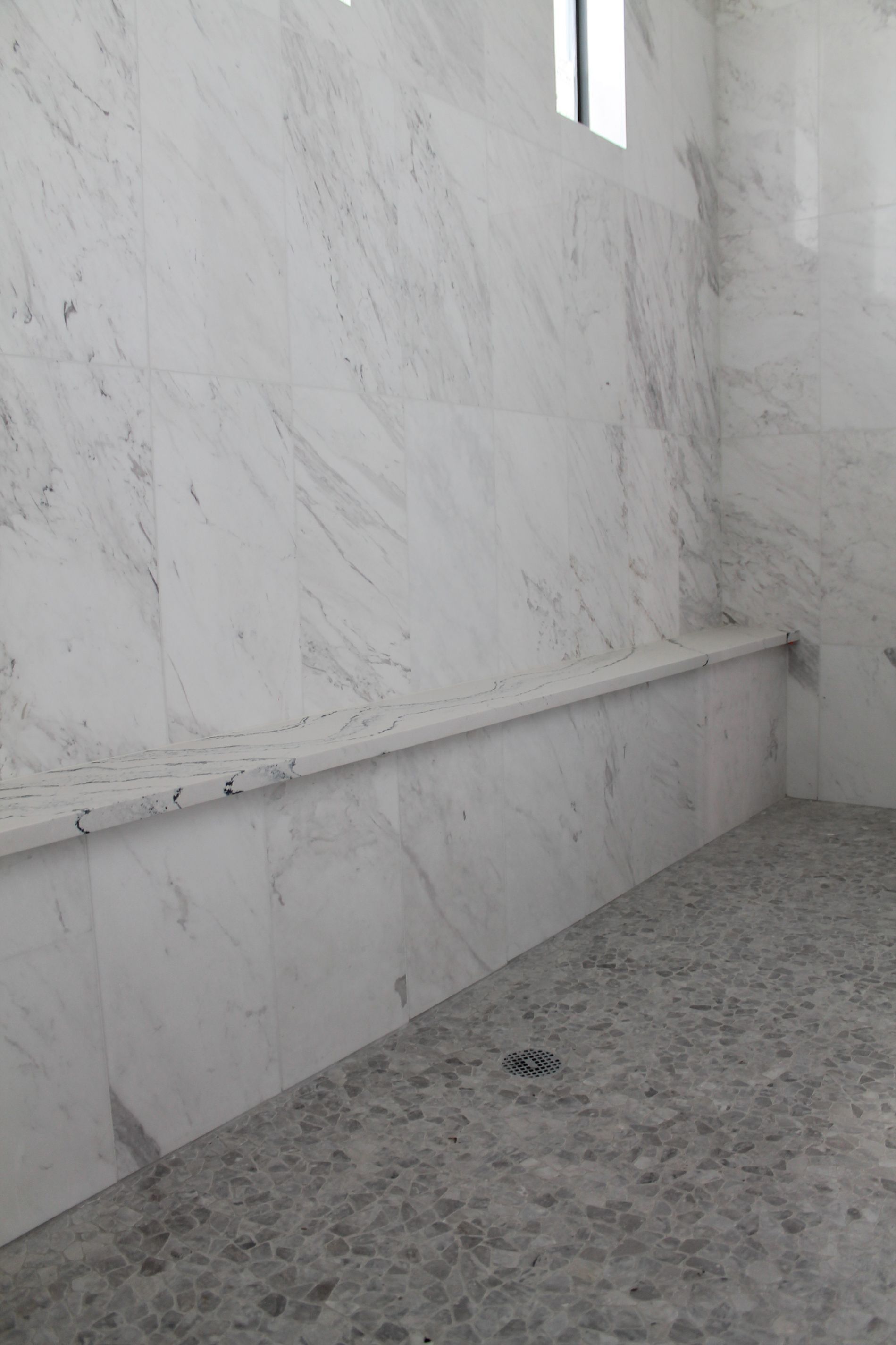A bathroom with marble walls and a bench in the shower.