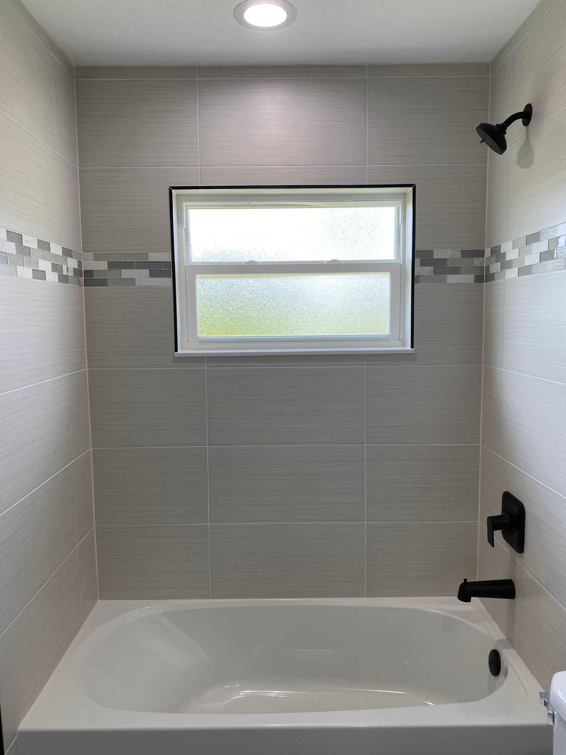A bathroom with a bathtub , shower , and window.
