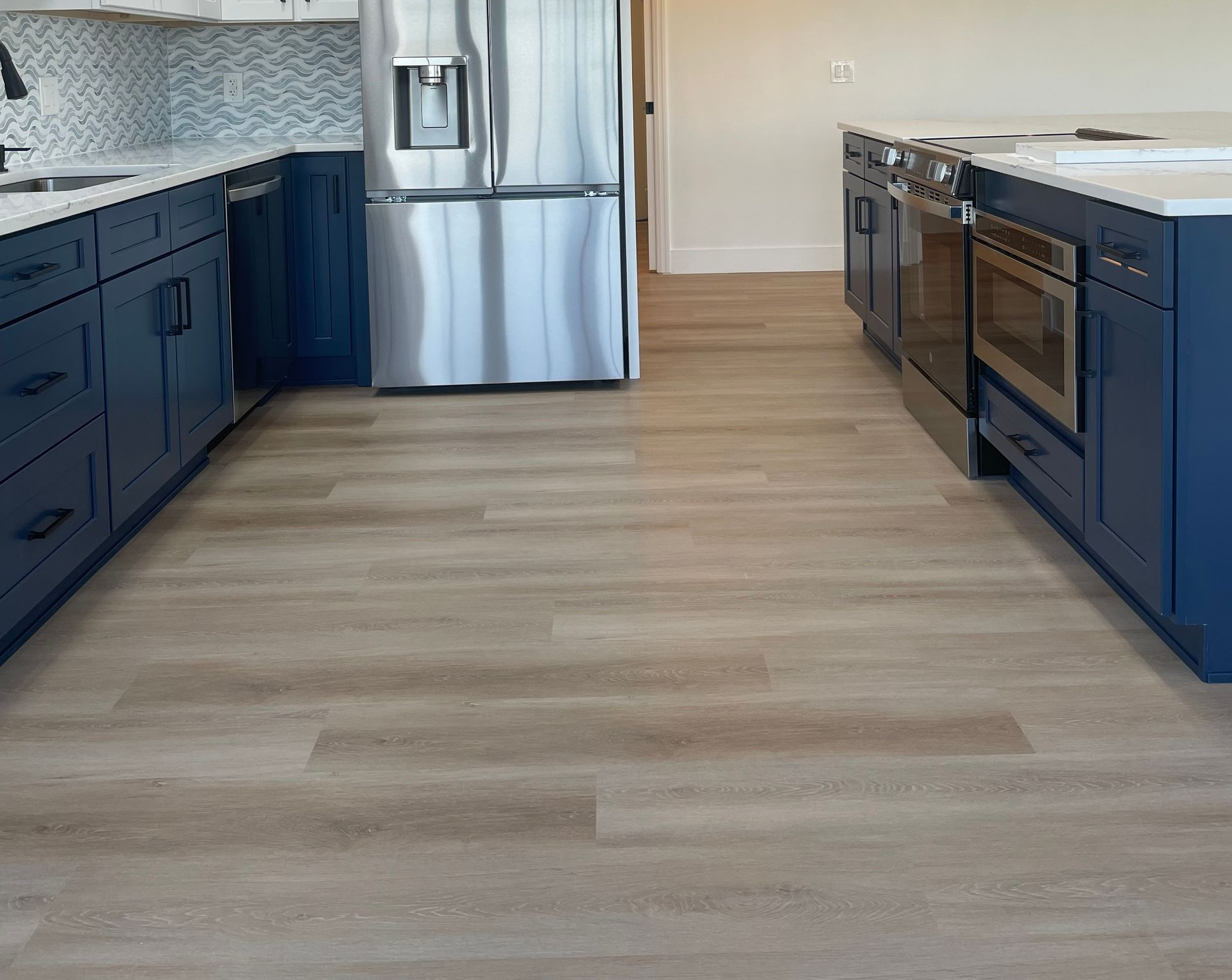 Modern kitchen with blue cabinets, tan light vinyl flooring brushed stainless steel accents and trim, double door fridge and blue backsplash