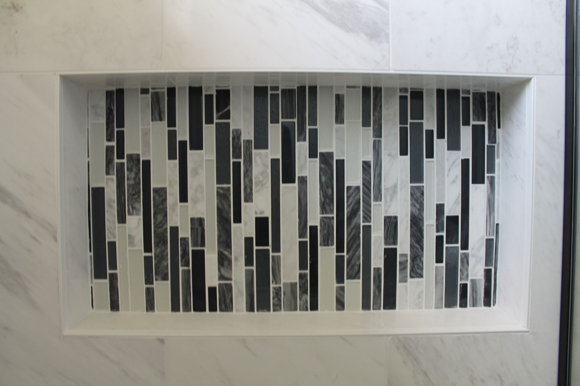 A shower niche with black and white tiles on a marble wall.