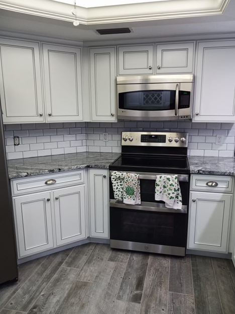 A kitchen with white cabinets , a stove , a microwave , and a refrigerator.