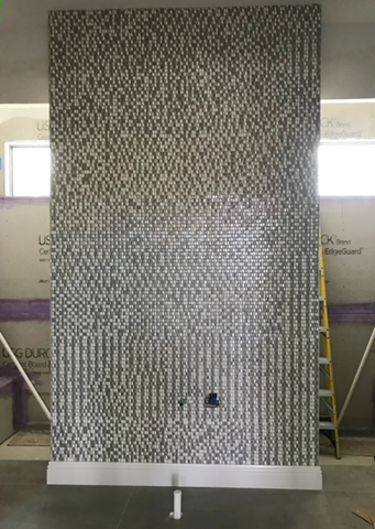 A large mosaic wall is being built in a bathroom.