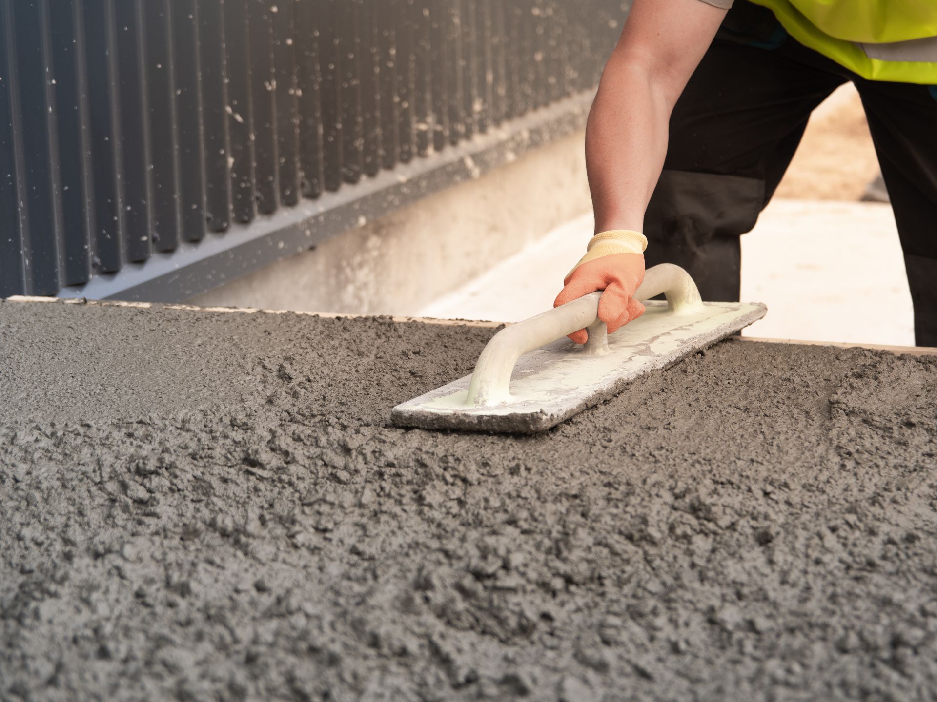 Male construction worker in gloves leveling concrete.
