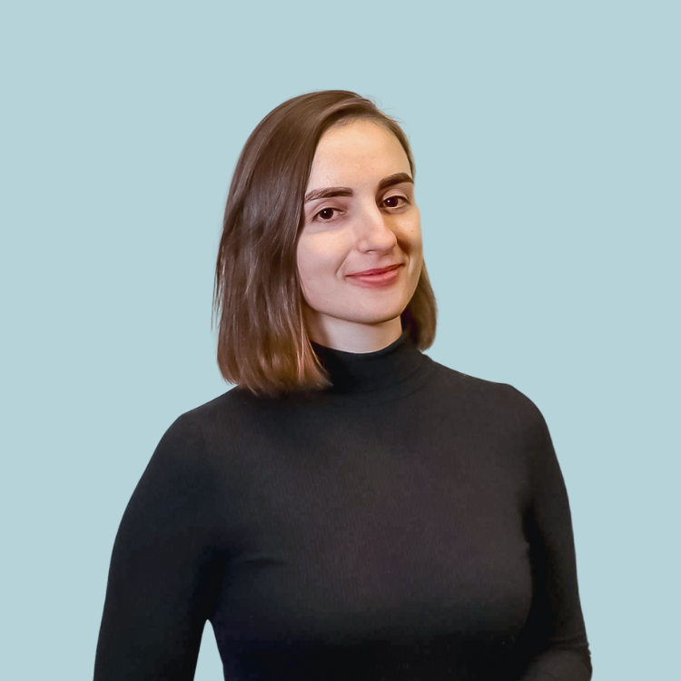 Woman with short brown hair, smiling, wearing a black turtleneck, against a light blue background.
