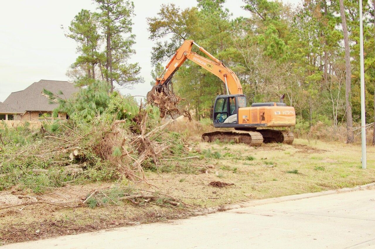 Orange excavator clearing brush near a residential area.