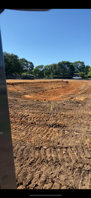 A construction site of a cleared, earthen area with trees in the distance under a blue sky.