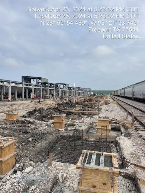 Construction site with exposed foundations and concrete forms near a train track in Freeport, TX.
