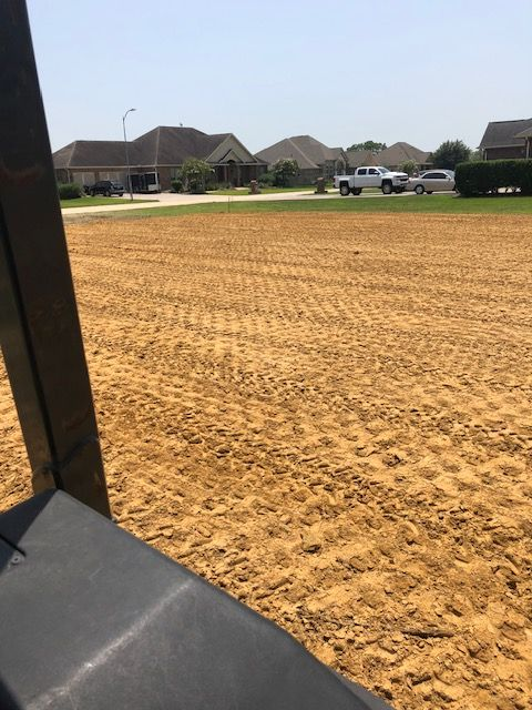 Brown sandy ground in the foreground with tire tracks; a suburban street and houses are in the background.